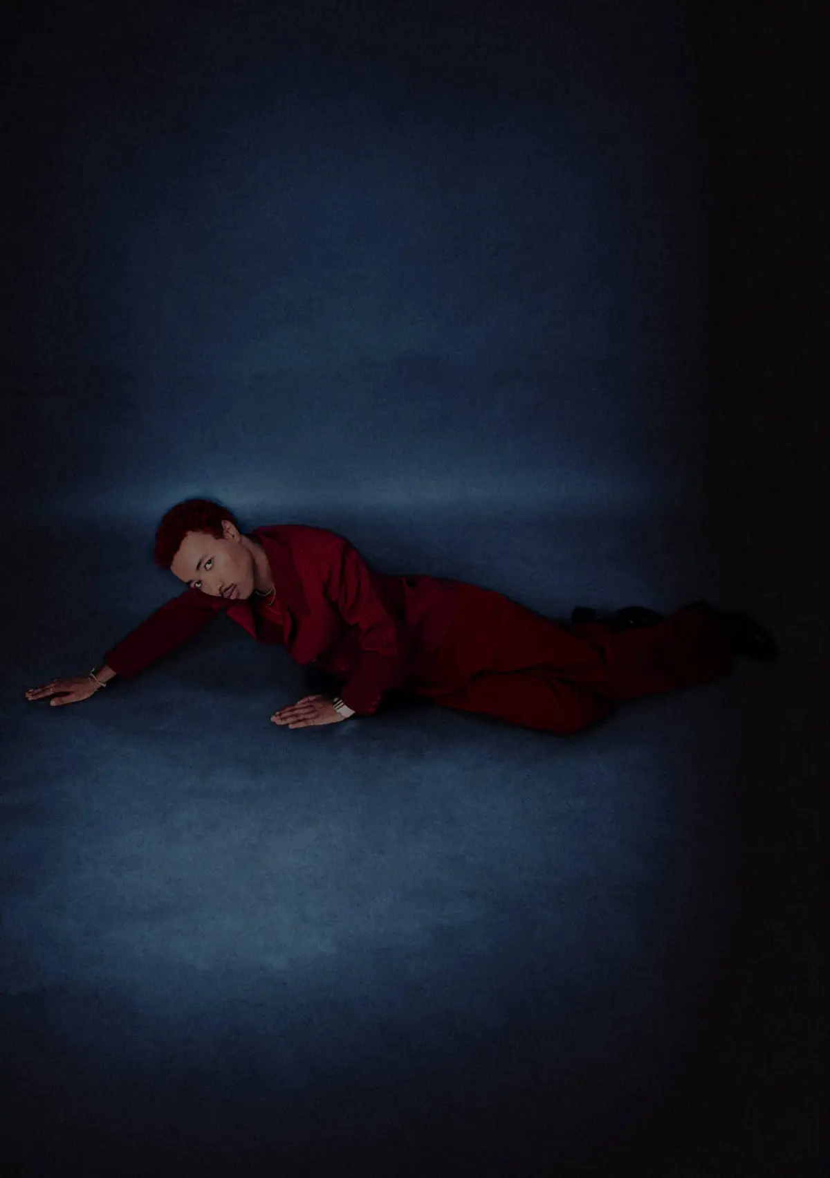 Person in a red suit lying on a blue floor, reaching forward with their left arm.